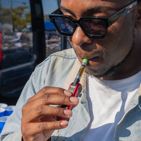 Person using a Hinge vape device outdoors with a blurred background