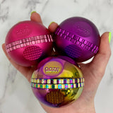 Holding a pink, purple, and rainbow saturn grinder in one hand