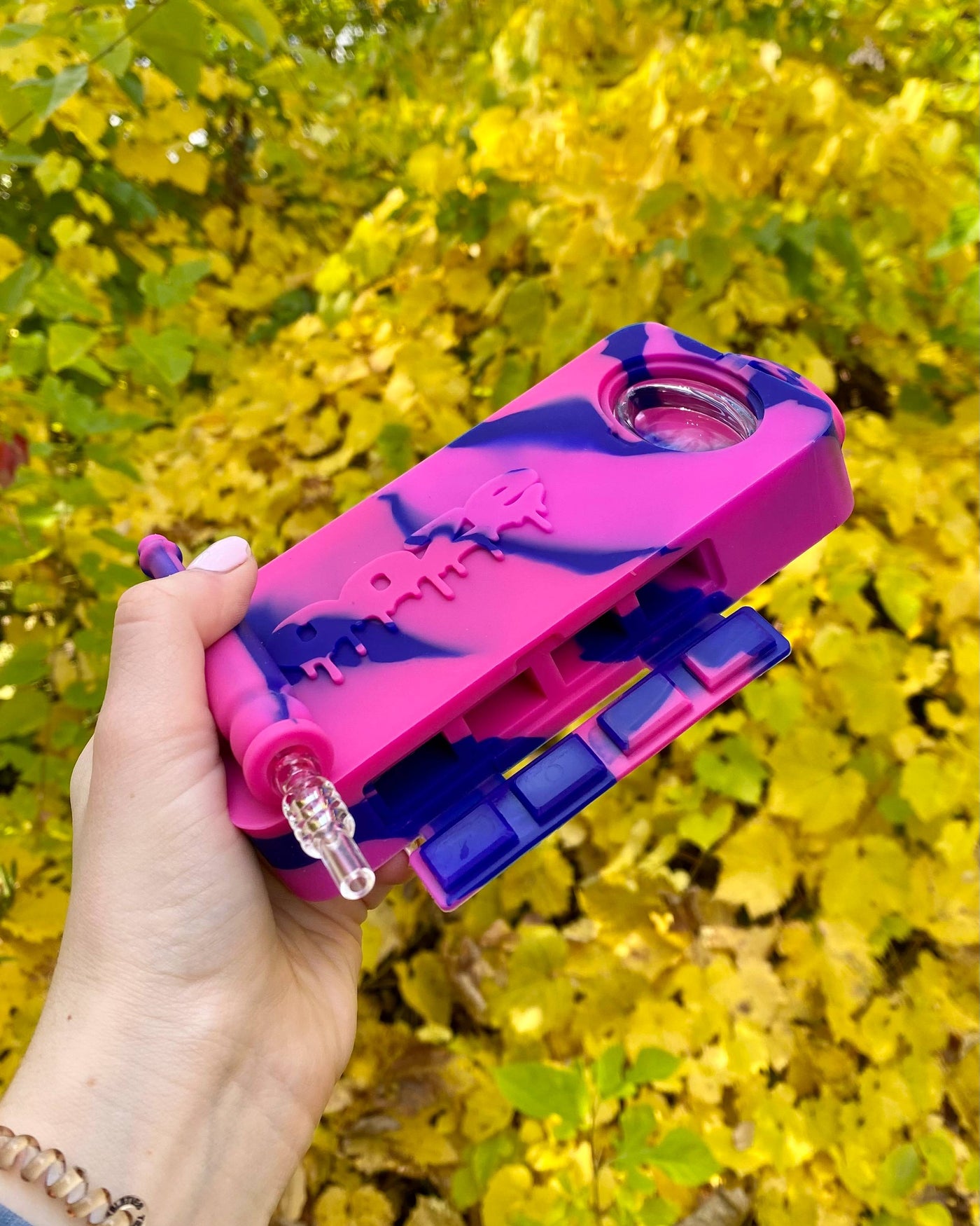 Holding a pink and purple Ooze slugger dab dugout outside with yellow leaves in the background