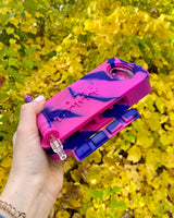 Holding a pink and purple Ooze slugger dab dugout outside with yellow leaves in the background
