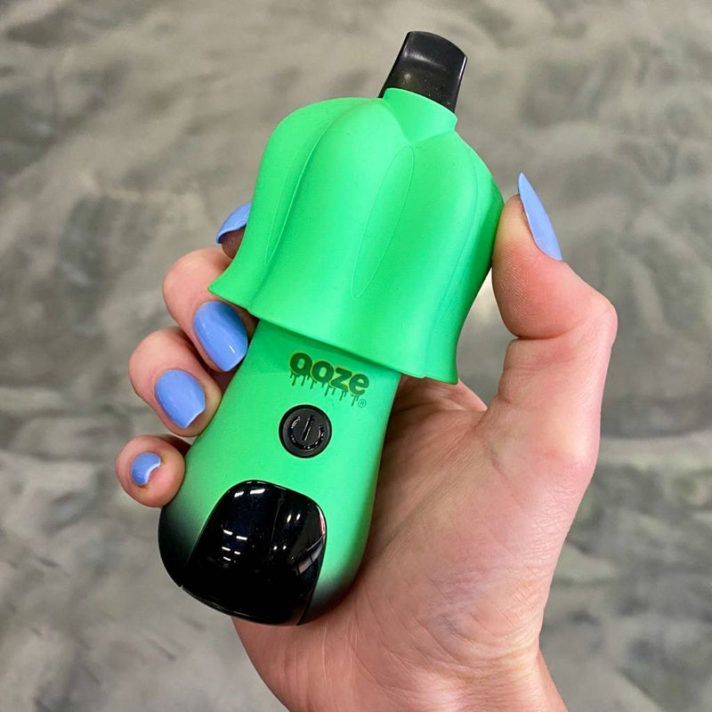 Hand holding green and black Ooze Shroom vape pen against a gray background