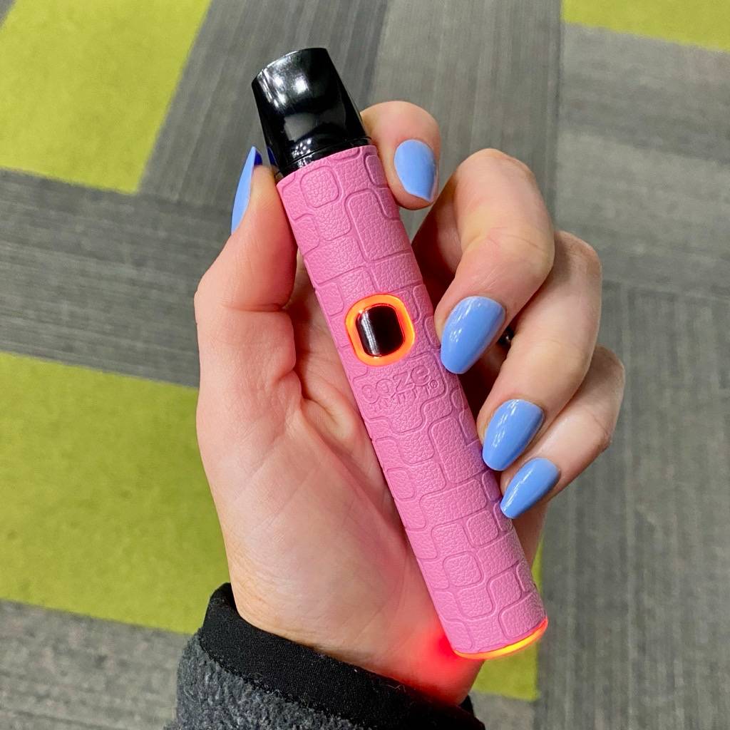 Hand holding a pink textured Pinch dry herb vape pen with a black top on a patterned surface