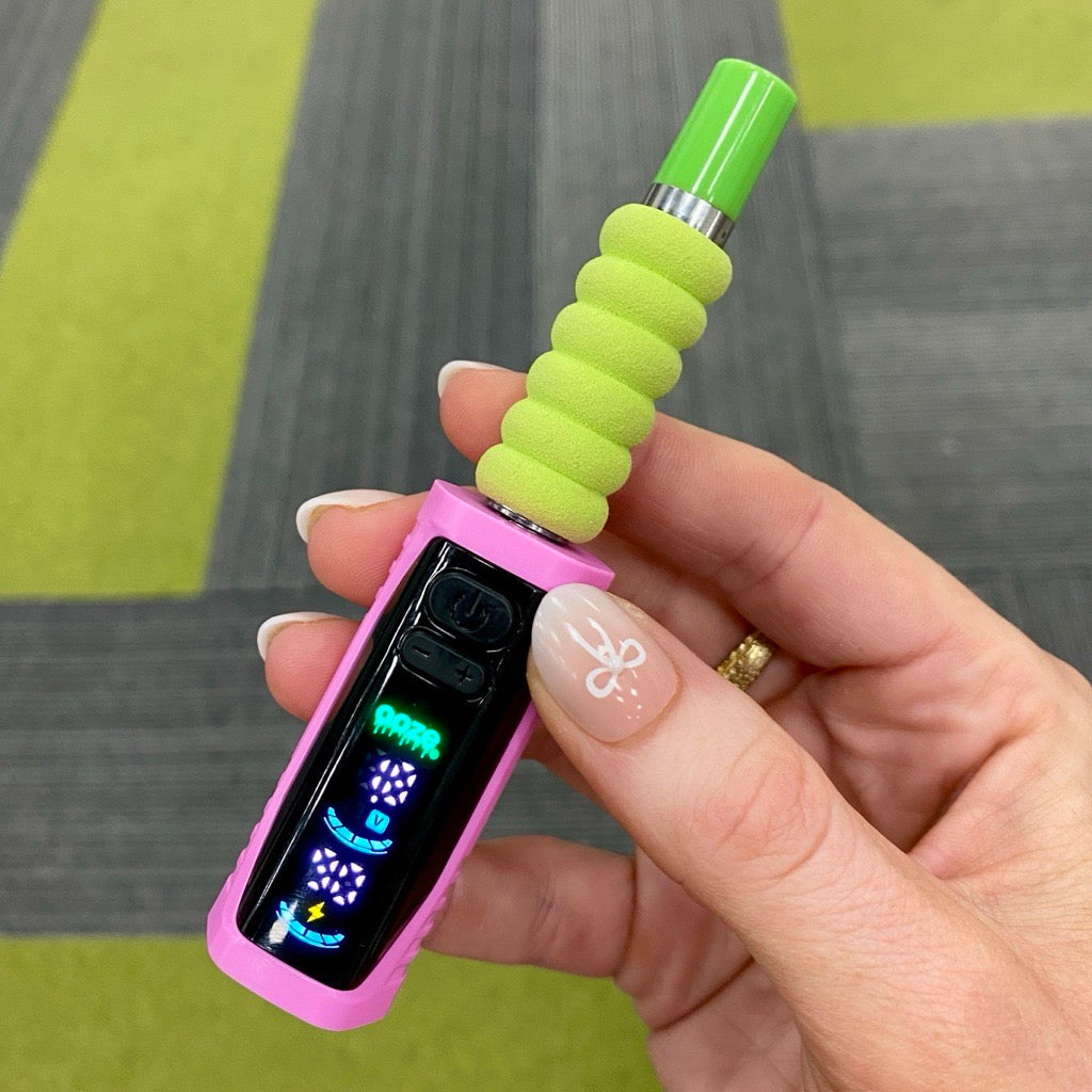 Close up shot of a hand holding the pink Ooze Runt Mini Battery with a cartridge with a green tip and cover connected and the screen turned on