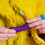 Person folding up a purple Hinge flick vape pen against a yellow furry background