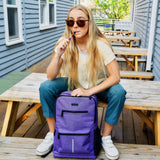 Girl taking a puff of a purple vape pen while opening her purple Ooze backpack and sitting at a picnic table