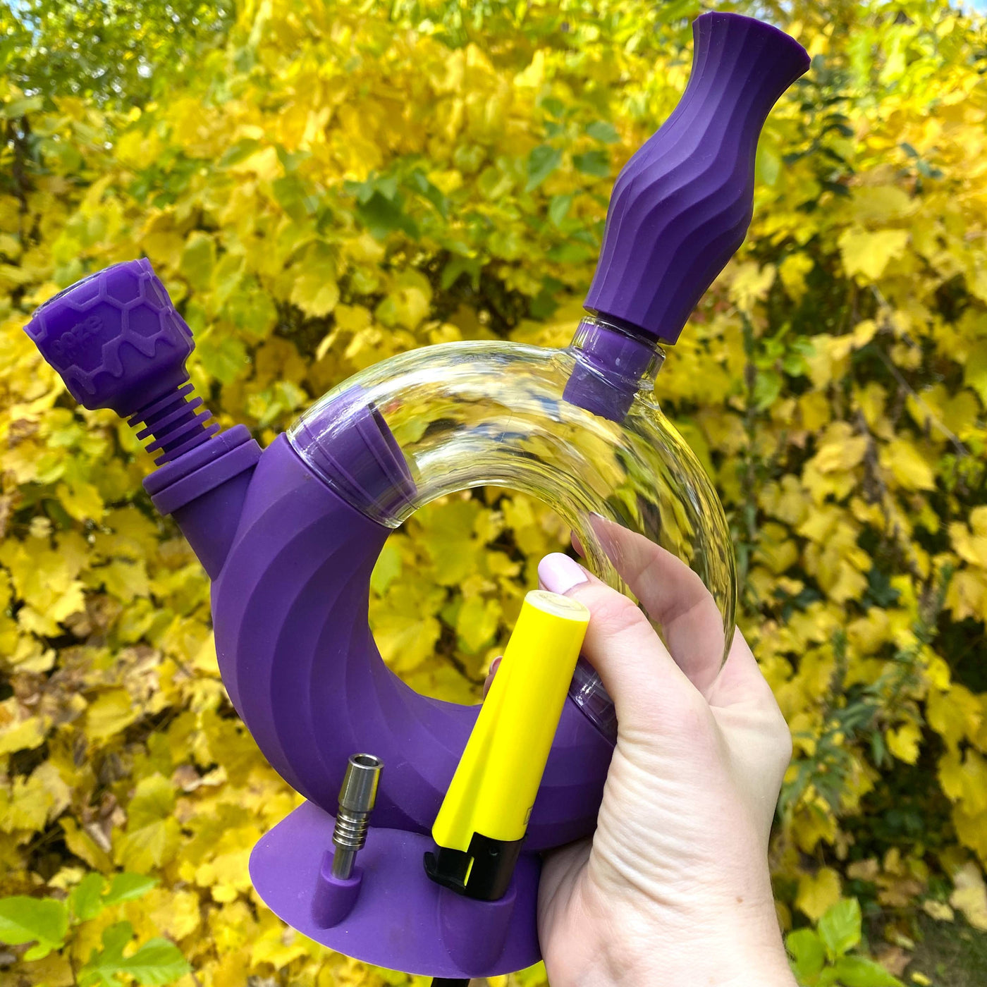 Purple Ooze Ozone water pipe is held outside with the armor bowl inserted and a yellow lighter in a slot on the side