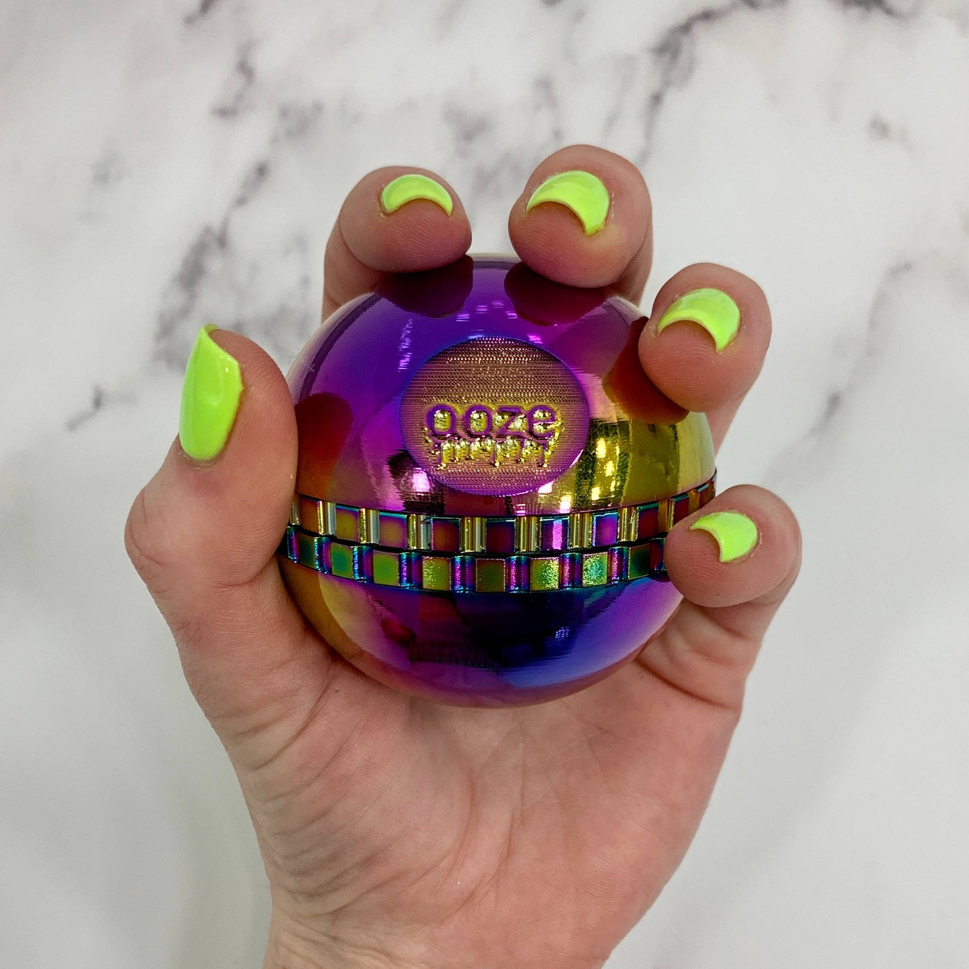 Holding a rainbow saturn grinder with neon green nails