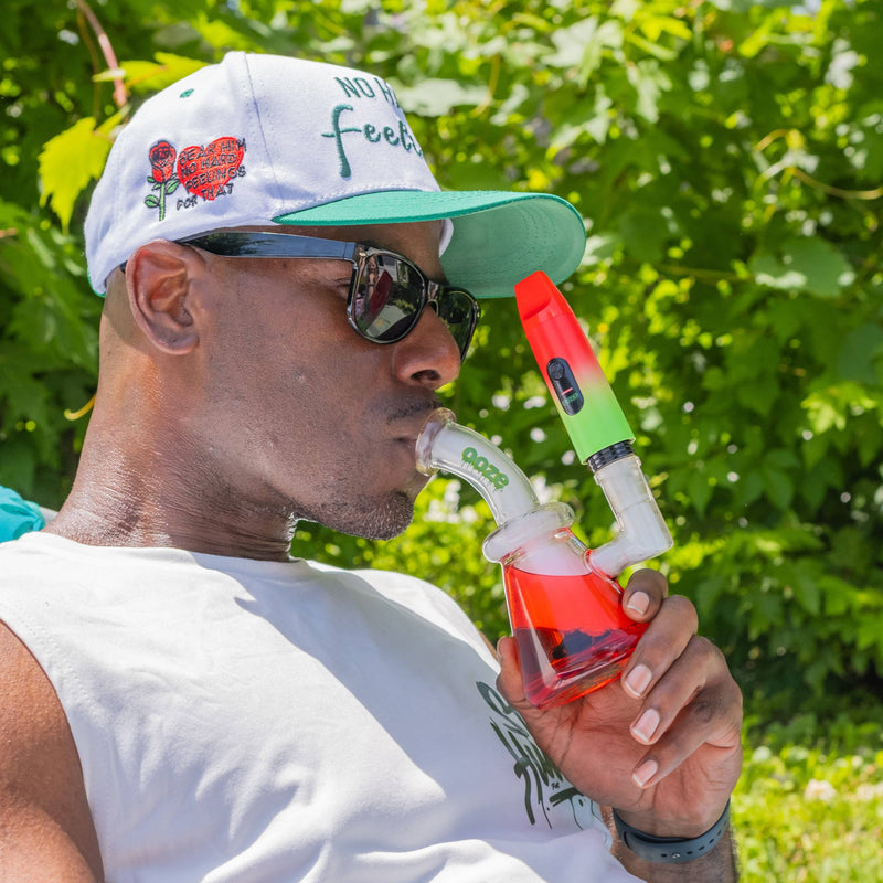 Man smoking from a colorful water pipe with greenery in the background