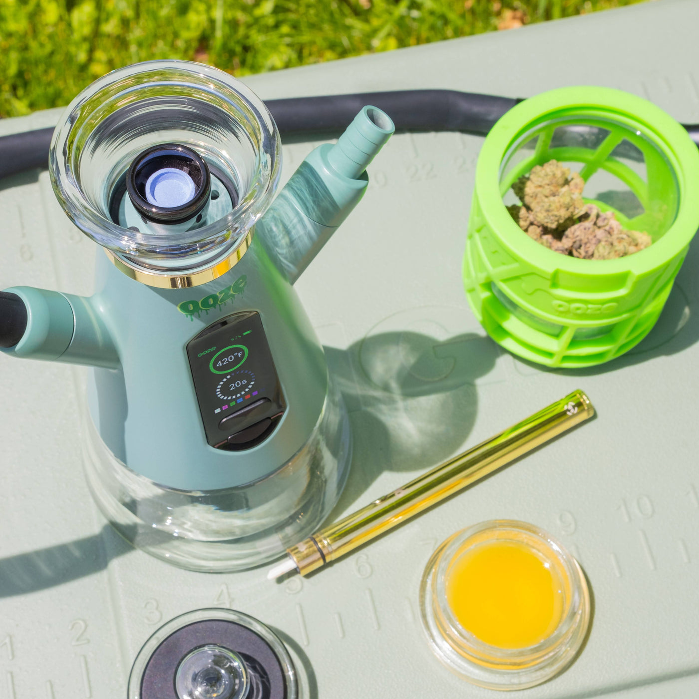 A mint Ooze Ripley dab rig hookah is shown from above with the atomizer visible, a jar of wax, a hot knife, and jar of wax also on the table.
