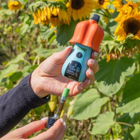 Person holding a Shroom vape, pulling the base out, with a sunflower in the background