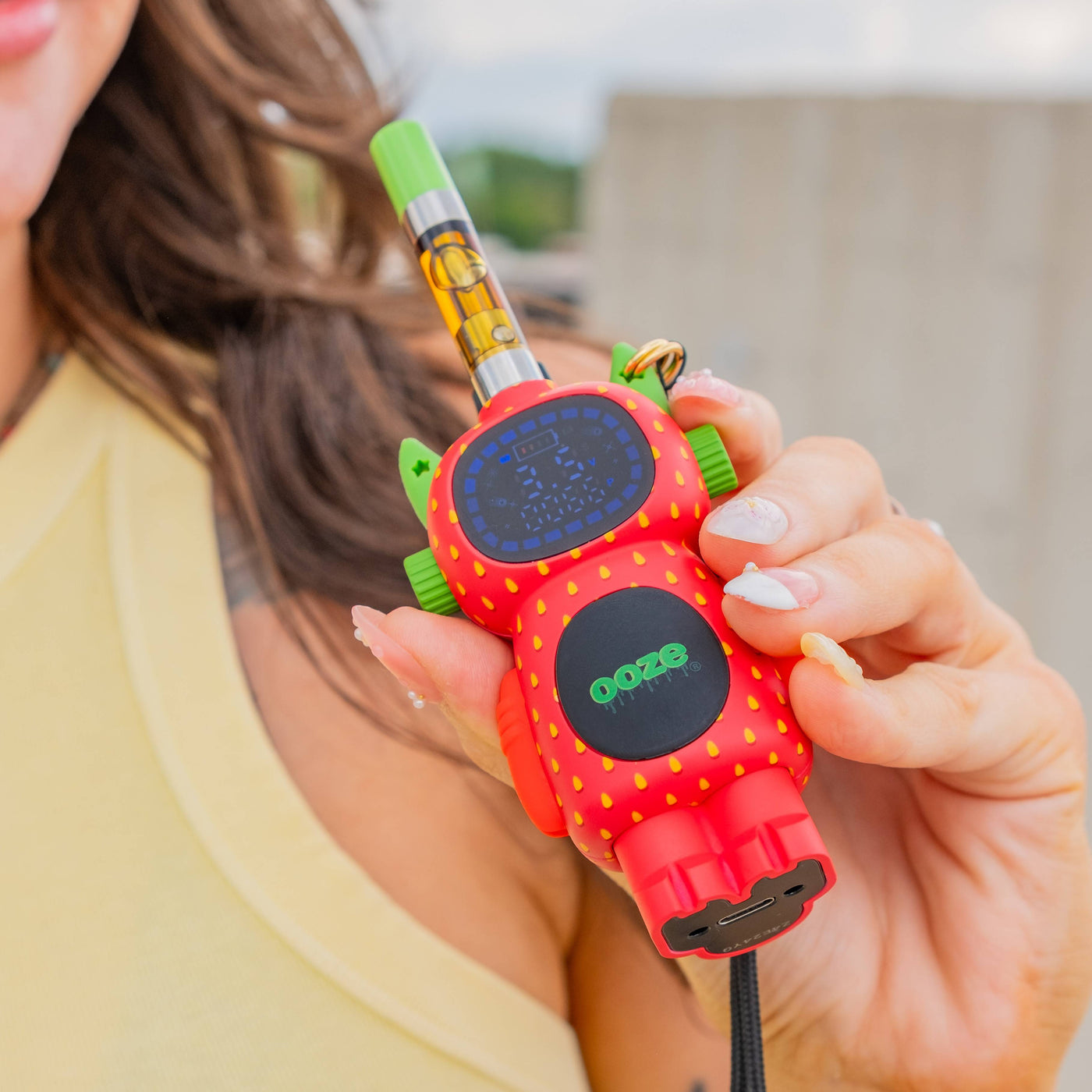 Close up of a woman holding a strawberry ooze Bot vape battery with a cartridge on top