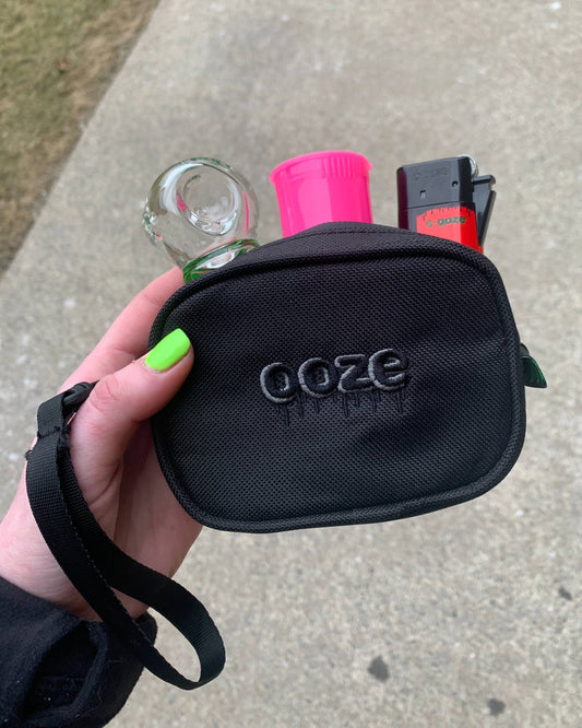 A girl holds a black Ooze Wristlet with a cryo bowl, pink pop top vial, and lighter inside