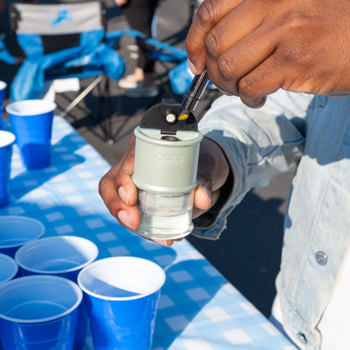 Close-up of a person using an ooze Hot Knife to load a dab into an electro barrel e-rig above a beer pong table with blue cups
