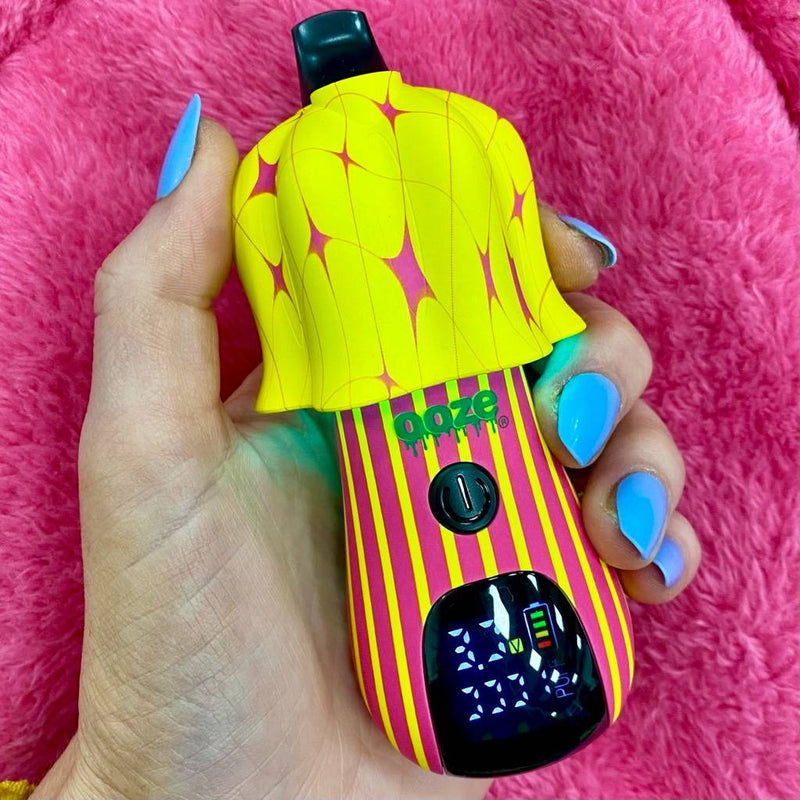 Person holding pink and yellow design Ooze Shroom vape battery against a pink fuzzy background
