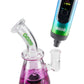 The rainbow Ooze Verge dry herb vape with the water pipe adapter cap attached is being inserted into the downstem of the purple Glyco bong.