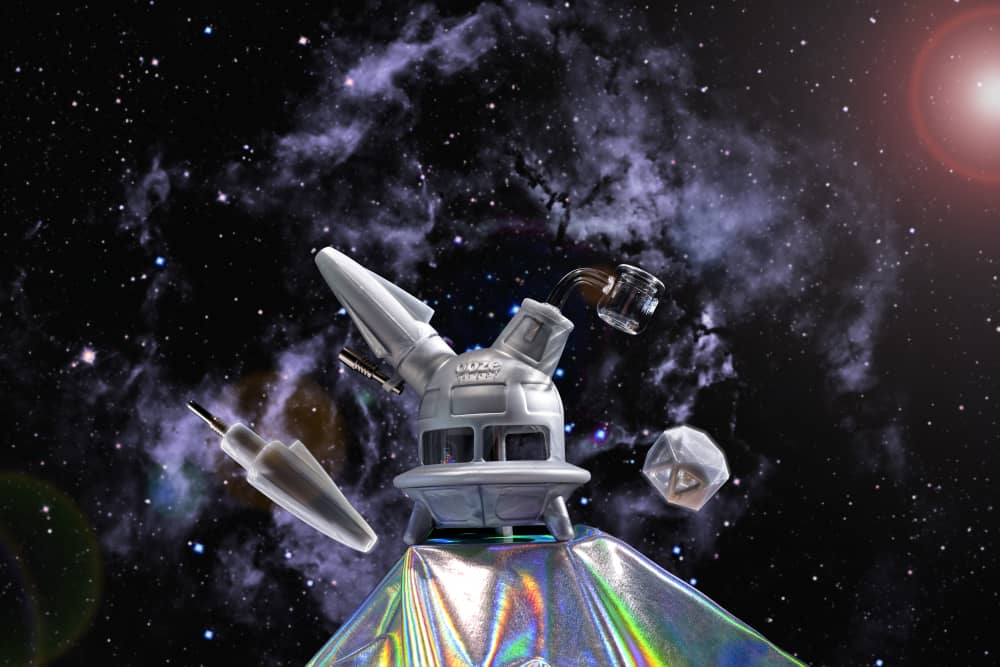 The stellar silver Ooze UFO is shown as a dab rig against a galaxy background with the dab straw and matching stash jar nearby