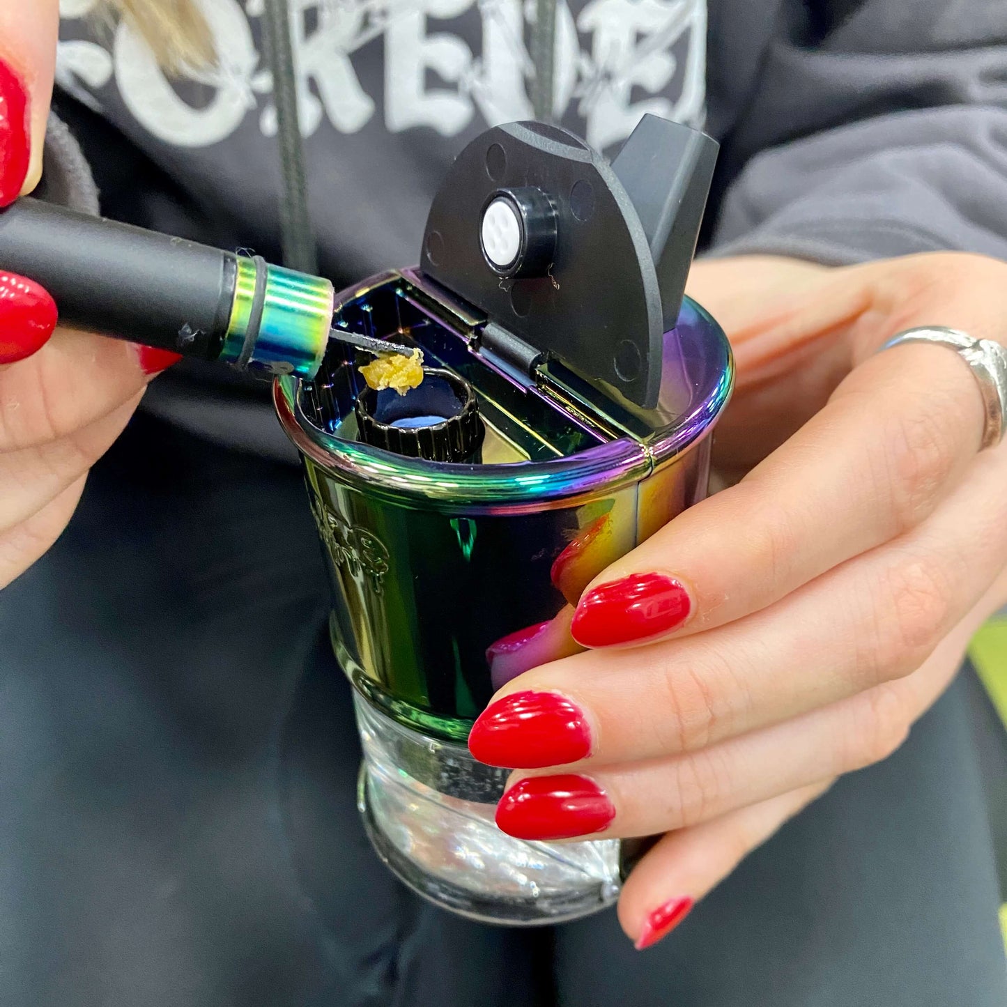 A girl is loading a dab into a rainbow Ooze Electro Barrel using a black Twist Hot Knife